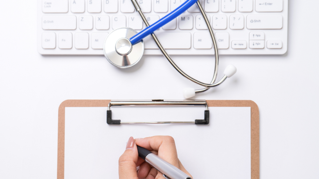 person writing on a clipboard in front of a stethoscope laying on a keyboard